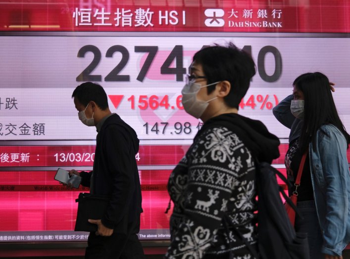 People wear protective masks as they walk past a panel displaying the Hang Seng Index during morning trading, following the outbreak of the new coronavirus in Hong Kong, China, March 13, 2020. REUTERS/Tyrone Siu